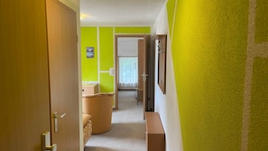 A hallway with a wooden door, a bench, and a view into a room with a window and a door.