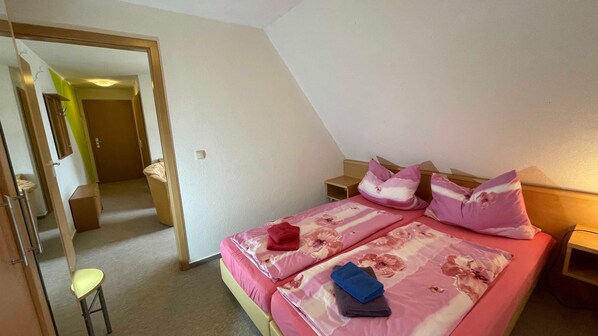 A bedroom with a bed, pillows, a nightstand, a chair, and a door leading to another room.