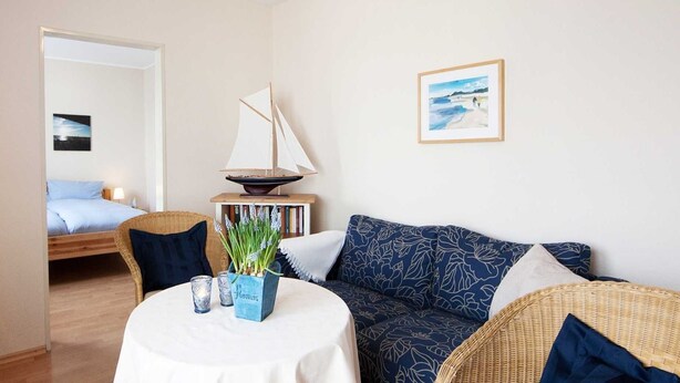 A compact living space with a kitchenette, a dining area with a table, a sofa, and a bookshelf. - 2-room app. No. 2-3, 34 m², 1st floor, balcony - Gästehaus Schäfersruh (Scharbeutz)