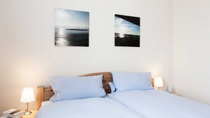 A neatly made bed with light blue bedding, two wall-mounted pictures depicting serene landscapes, and bedside lamps on either side. - 2-room app. No. 2-3, 34 m², 1st floor, balcony - Gästehaus Schäfersruh (Scharbeutz)