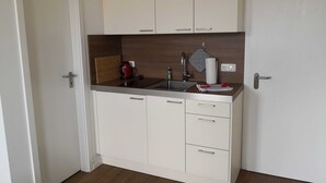 Una kitchenette compacta con un lavamanos, un hervidor y una pequeña encimera.