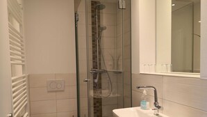 Un baño moderno con ducha acristalada, lavabo blanco y retrete.