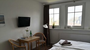 Habitación de hotel con dos camas, un escritorio con silla, televisión y ventana con cortinas.