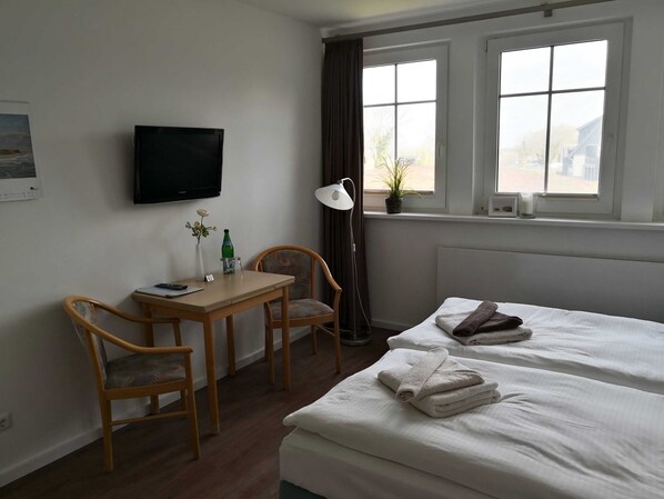 A hotel room with two beds, a desk with a chair, a TV, and a window with curtains.