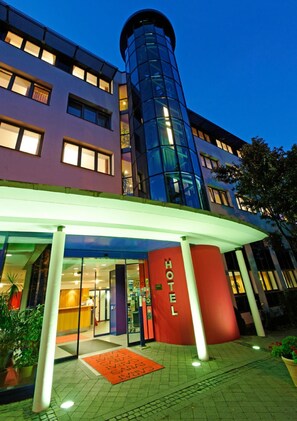 L'ingresso di un hotel dal design moderno, con facciata in vetro e insegna rossa.