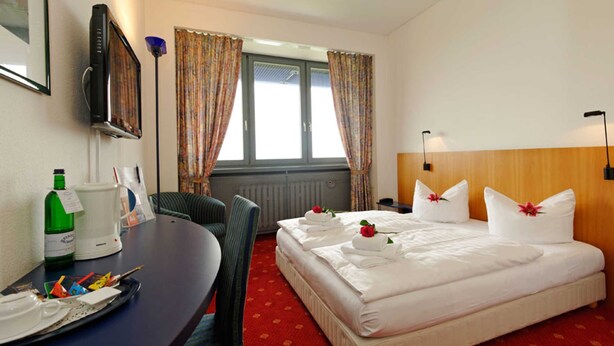 Habitación de hotel con cama, escritorio con silla, televisor y ventana con cortinas.