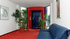 Vestíbulo de hotel con alfombra roja, un sofá azul y plantas en macetas.