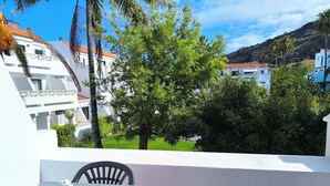 A balcony with a table and chairs, overlooking a garden with trees and buildings. - Amelia Cancajos: Comfort Swimming pool and beach nearby (Breña Baja)