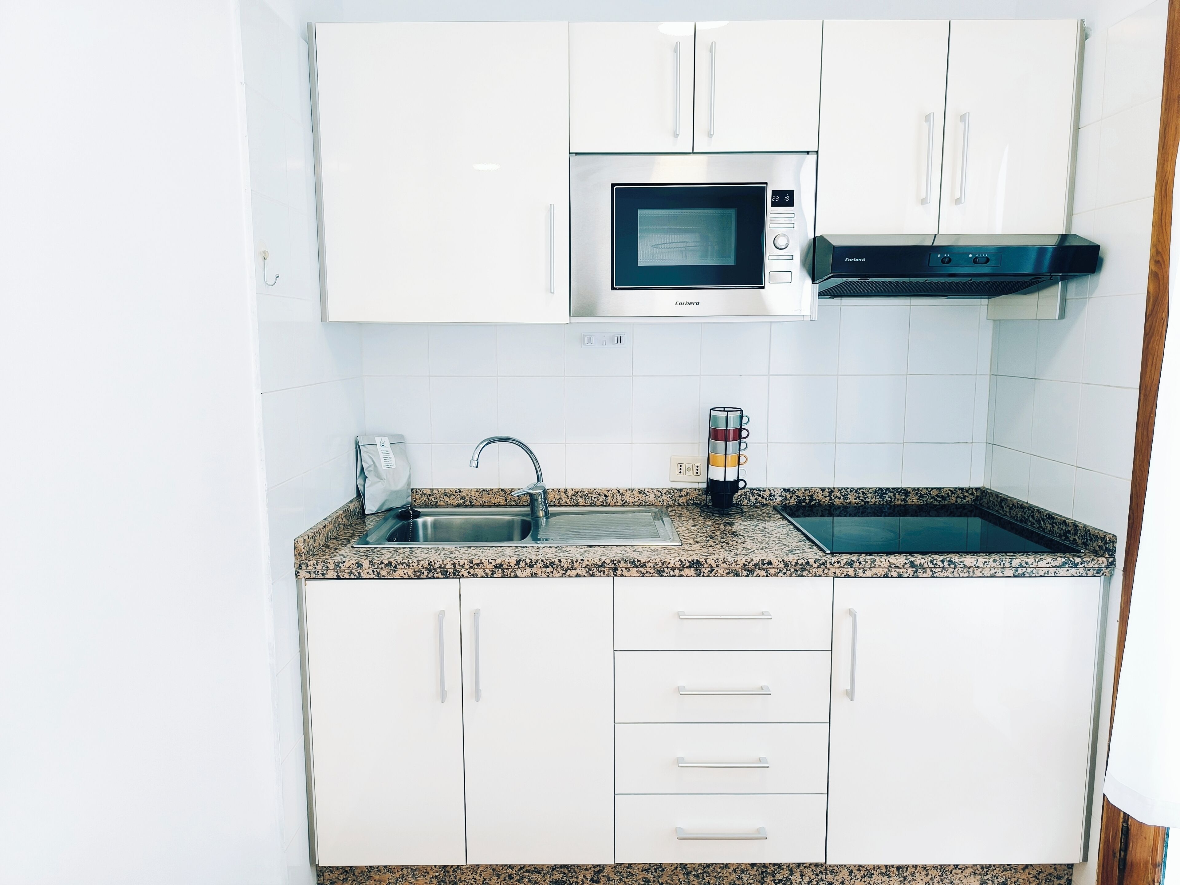 A modern kitchen with white cabinets, a stainless steel sink, a microwave, and a coffee maker.