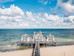 A waterfront hotel with a pier extending into the sea, featuring multiple buildings with large windows and a central tower.