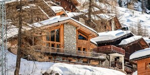 A multi-story wooden lodge with stone accents, balconies, and a snowy landscape.