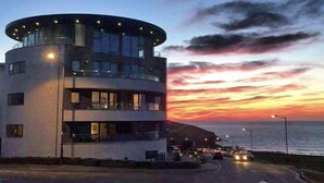 Un edificio moderno con un techo circular, ventanas amplias y vista al mar al atardecer.