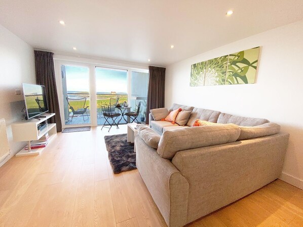 A modern living room with a sofa, a TV, and a view of the outdoors through a glass door.