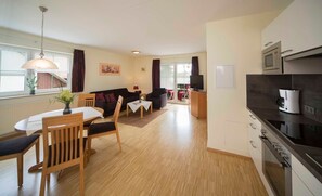 A modern living room with a dining area, a kitchen with a coffee machine, and a TV.