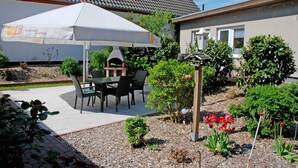 A patio with a table and chairs under a white umbrella, surrounded by potted plants and a small garden.