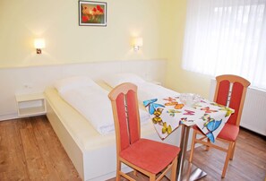 A hotel room with a bed, a table with a butterfly tablecloth, two red chairs, and a small shelf under the bed.