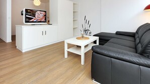 Ein modernes Wohnzimmer mit Flachbildfernseher, einem weißen Schrank, einer schwarzen Ledersofa und einem kleinen weißen Tisch.