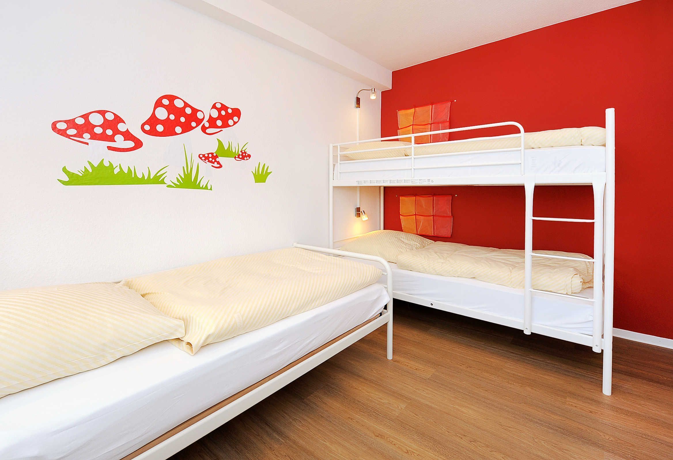 Une chambre avec des lits superposés, un mur rouge et un motif de champignons décorant un autre mur.