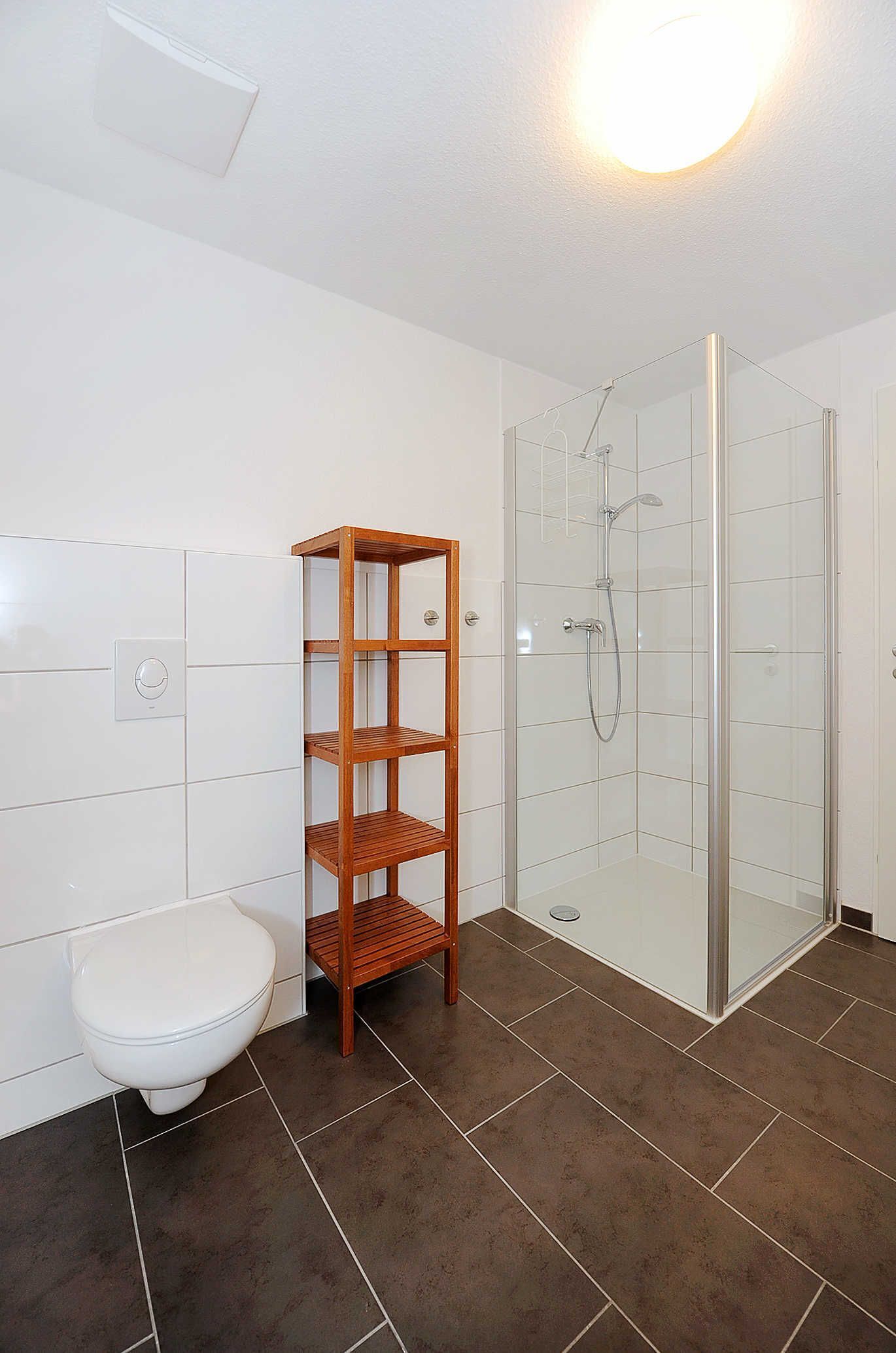 A bathroom with a toilet, a wooden shelf, and a glass-enclosed shower.