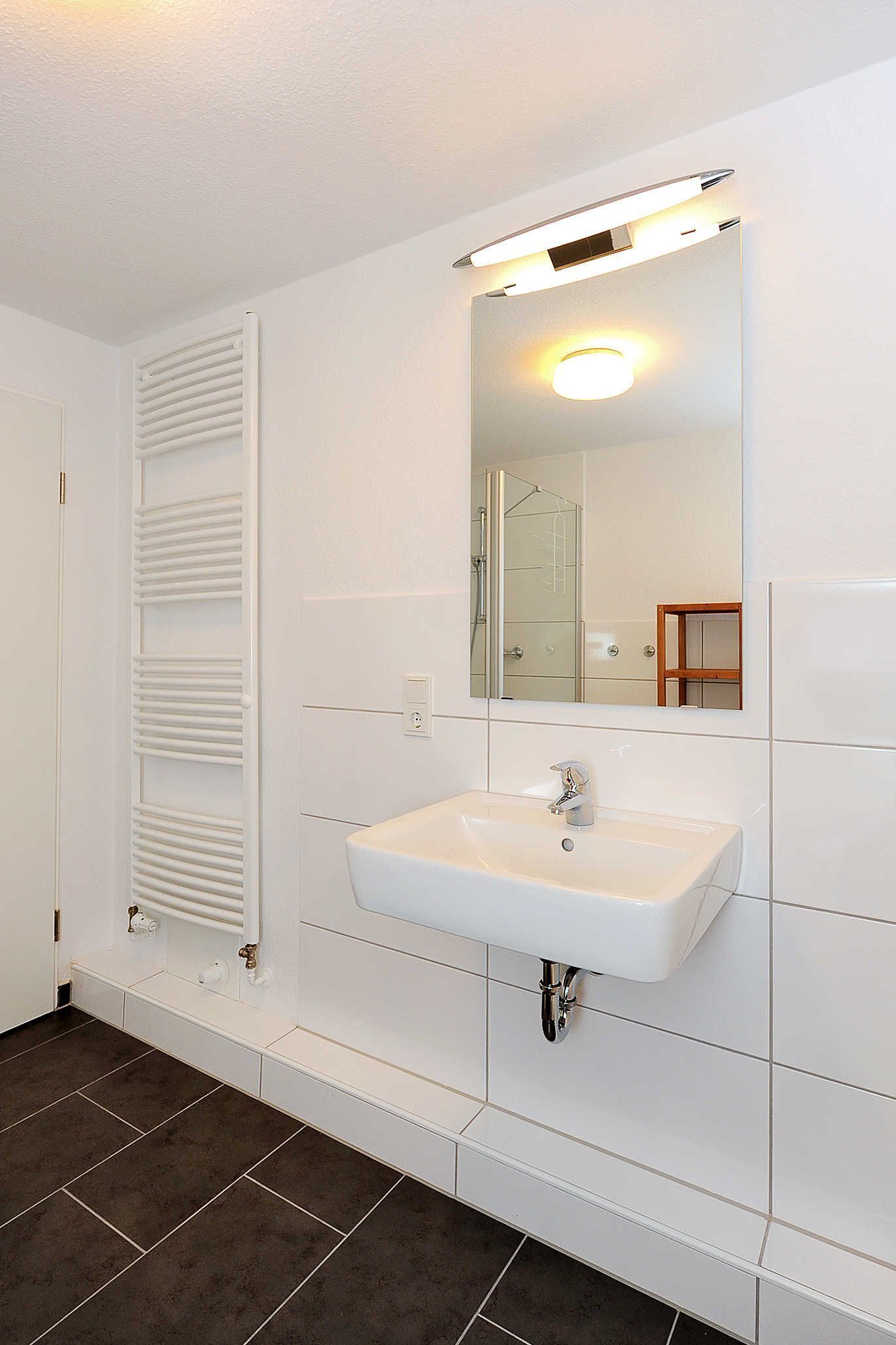 Un baño con un lavamanos blanco, un espejo y un toallero.