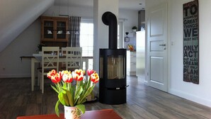 En hyggelig stue med en sort brændeovn, et spisebord med en vase fyldt med tulipaner, og et køkken i baggrunden.