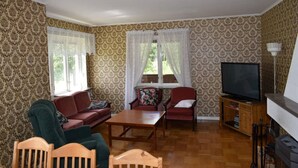 A living room with patterned wallpaper, a television, a fireplace, and a wooden coffee table. - Magnificent house with big garden (Munkfors)