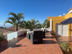 Une terrasse sur le toit, aménagée avec du mobilier d’extérieur, des plantes en pot et offrant une vue sur la mer.