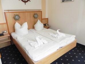 Ein Doppelbett mit weißen Leinen und Handtüchern, die zu einem Schwan geformt sind. Zwei Nachttische, einer mit einem Telefon und der andere mit einer Kamera.