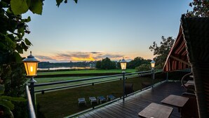 Eine Terrasse mit Sitzgelegenheit und zwei beleuchteten Laternen, mit Blick auf eine Rasenfläche und einen Sonnenuntergang.