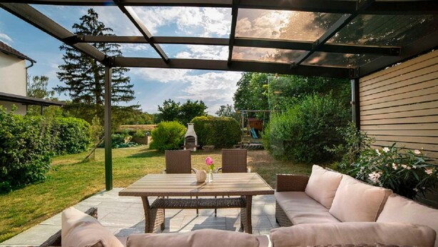 A covered patio with a table and wicker furniture, surrounded by greenery and a barbecue grill. - Vacation apartment - Kur & Golf Ferienwohnungen Wattenbach (Bad Windsheim)