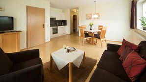 A living room with a sofa, a coffee table, and a TV. There is a dining area with a table and chairs. - Vacation apartment - Kur & Golf Ferienwohnungen Wattenbach (Bad Windsheim)