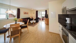 A modern living room with a dining area, a kitchen with a coffee machine, and a TV. - Vacation apartment - Kur & Golf Ferienwohnungen Wattenbach (Bad Windsheim)