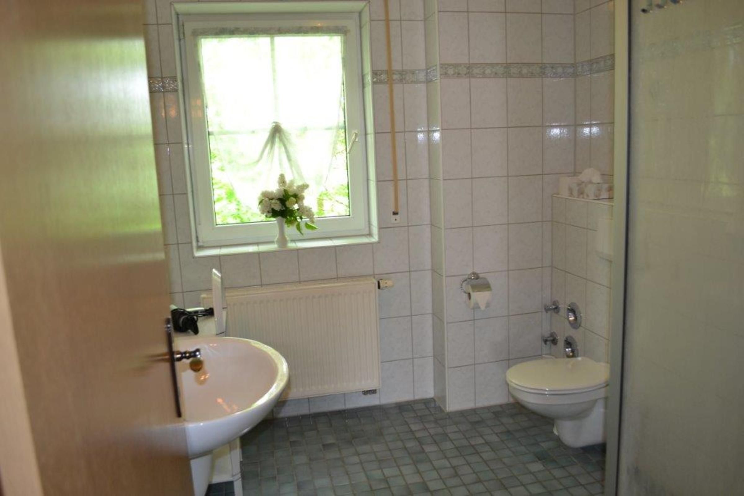 Een badkamer met een wastafel, toilet en een raam met uitzicht op groen.