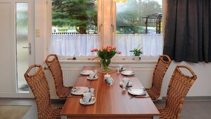Un comedor con una mesa de madera preparada para cuatro, rodeado de sillas de mimbre, un florero con tulipanes rojos y vistas a árboles a través de una ventana.
