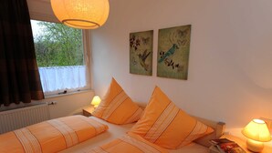 Una cama doble con ropa de cama naranja y almohadas a rayas, una mesita de noche con lámpara, y dos cuadros con motivos de mariposas.