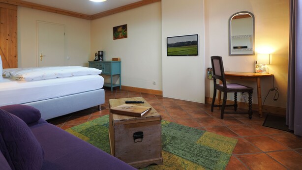 Un dormitorio con cama, escritorio, silla, cómoda y un pequeño cofre de madera.