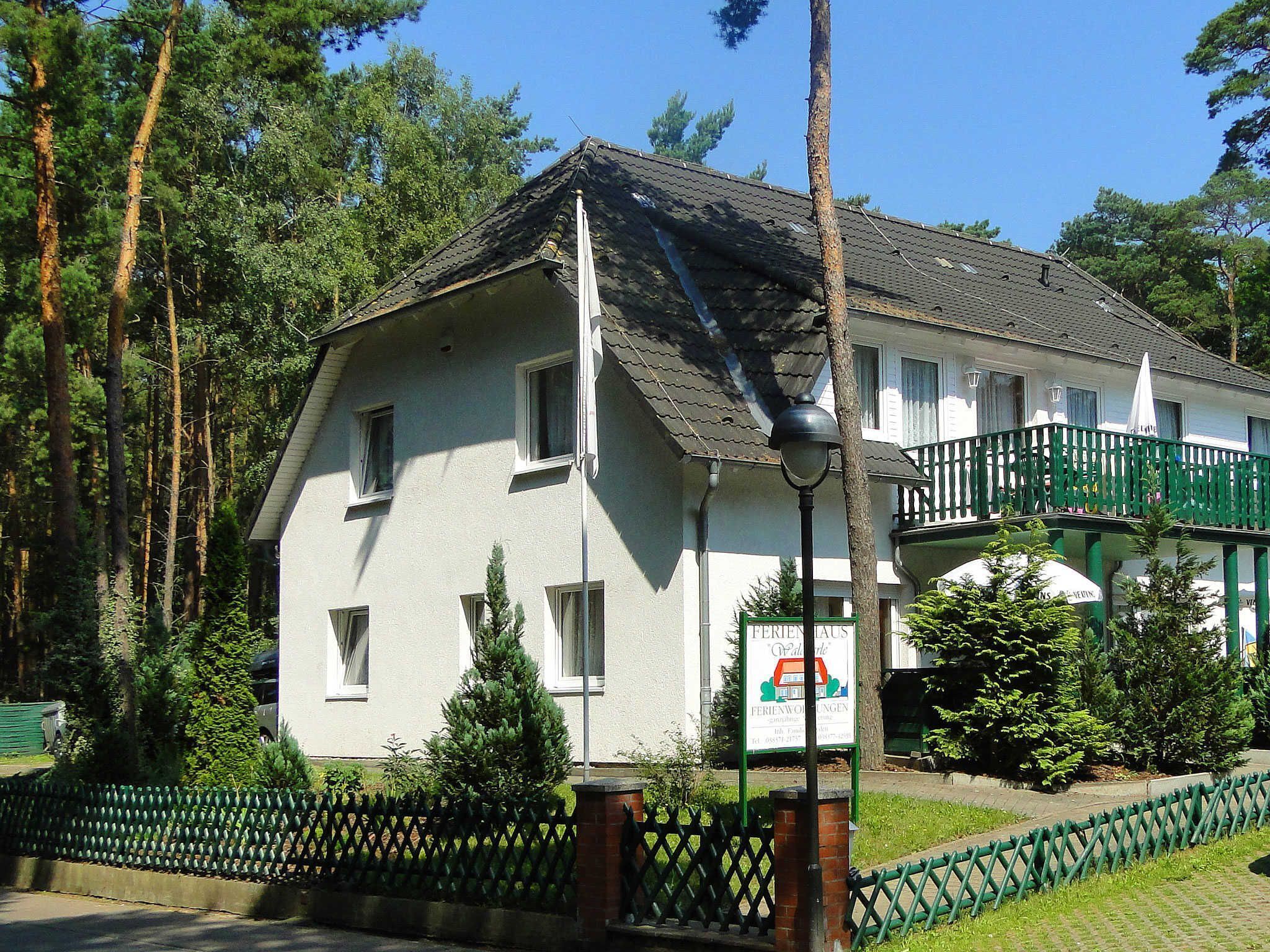 A two-story building with a balcony, surrounded by trees and a green fence.
