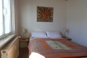 Une chambre à coucher avec un lit, deux tables de chevet, un radiateur et une fenêtre avec des stores.