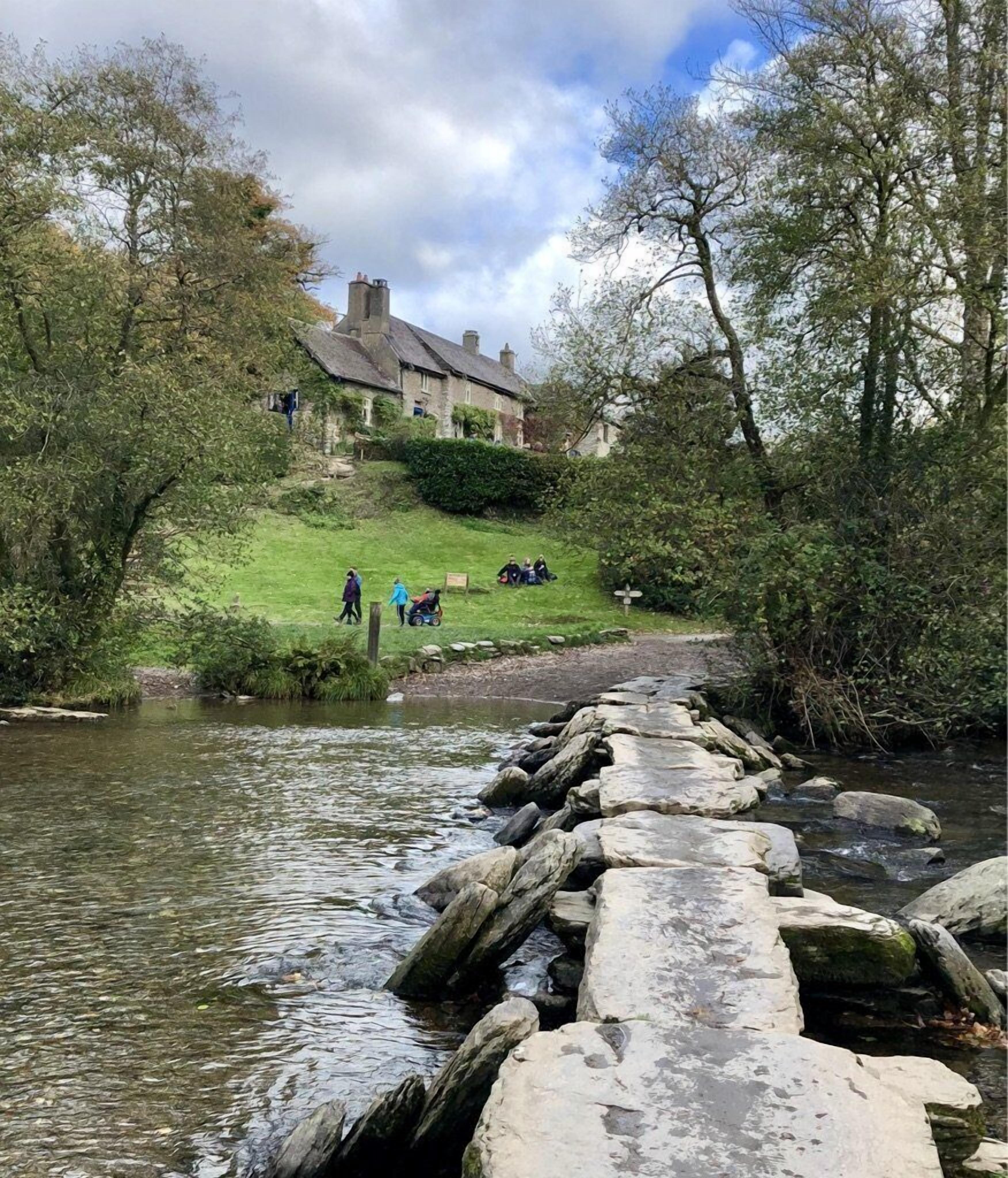 A stone bridge over a river with a grassy embankment and a building in the background.