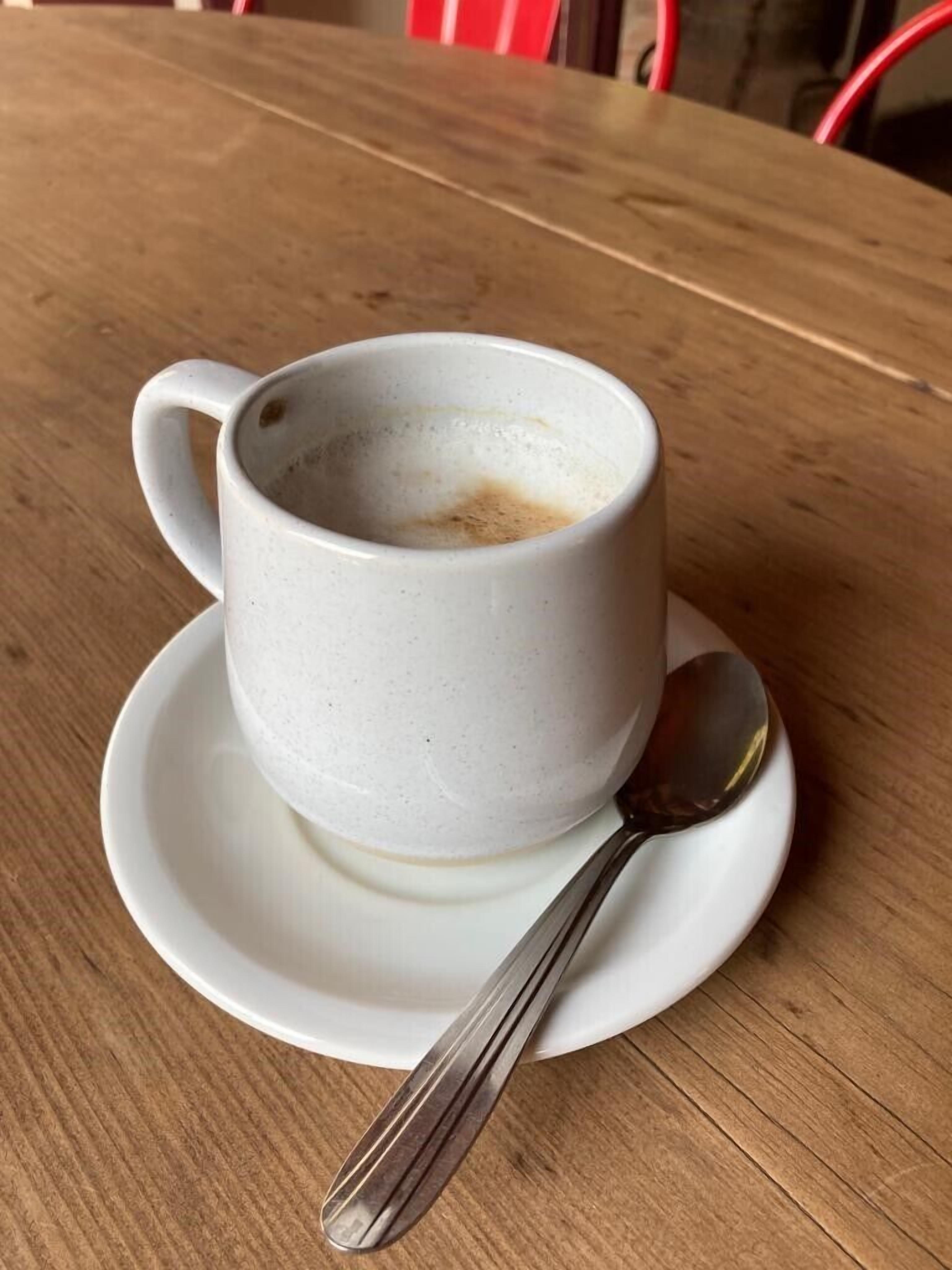 Une tasse en céramique blanche, avec une cuillère posée sur une soucoupe, est placée sur une table en bois.