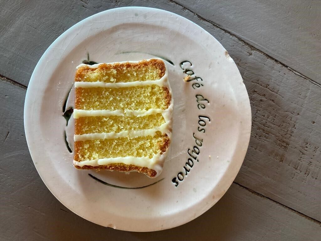 Una porción de pastel amarillo con glaseado blanco sobre un plato blanco con texto.