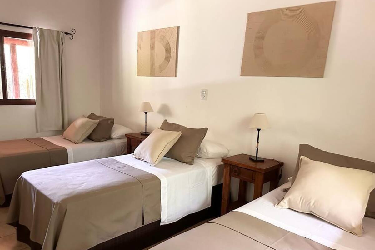 A hotel room with two single beds, each with a bedside table and lamp, and a window with curtains.