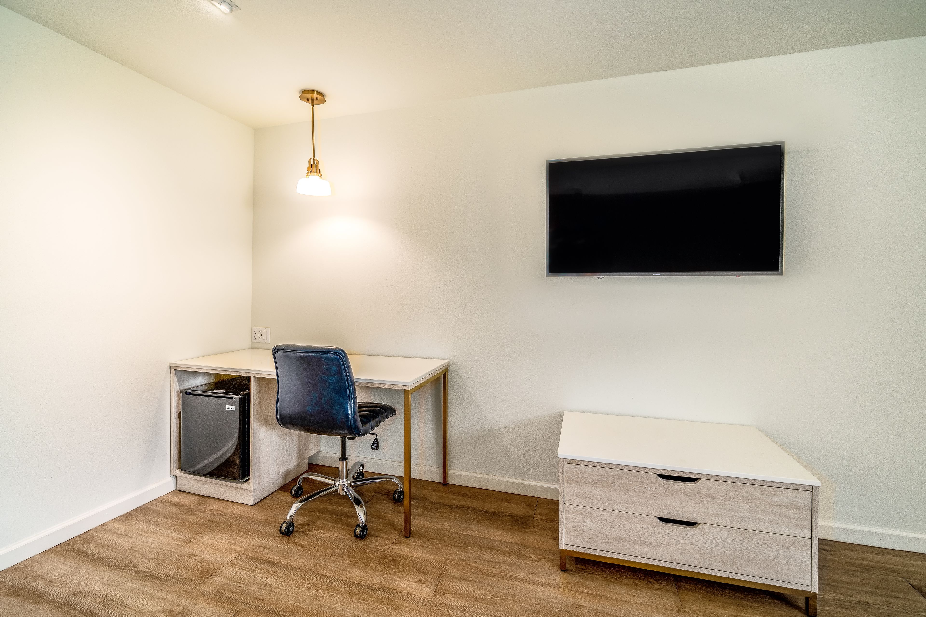 Een kleine, goed verlichte kamer met een bureau, stoel en een aan de muur bevestigde televisie.