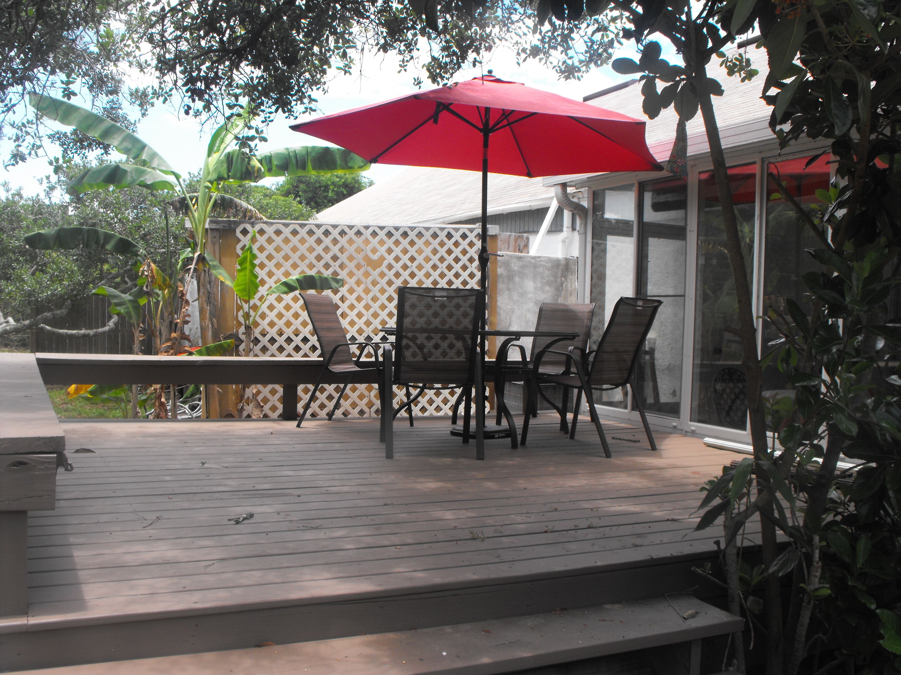 Een terras buiten met een tafel, stoelen, een rode parasol en een houten terras.