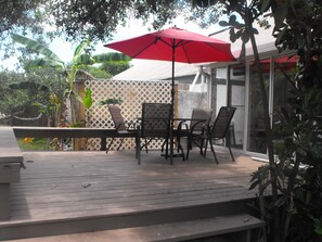 An outdoor patio with a table and chairs, a red umbrella, and a wooden deck.