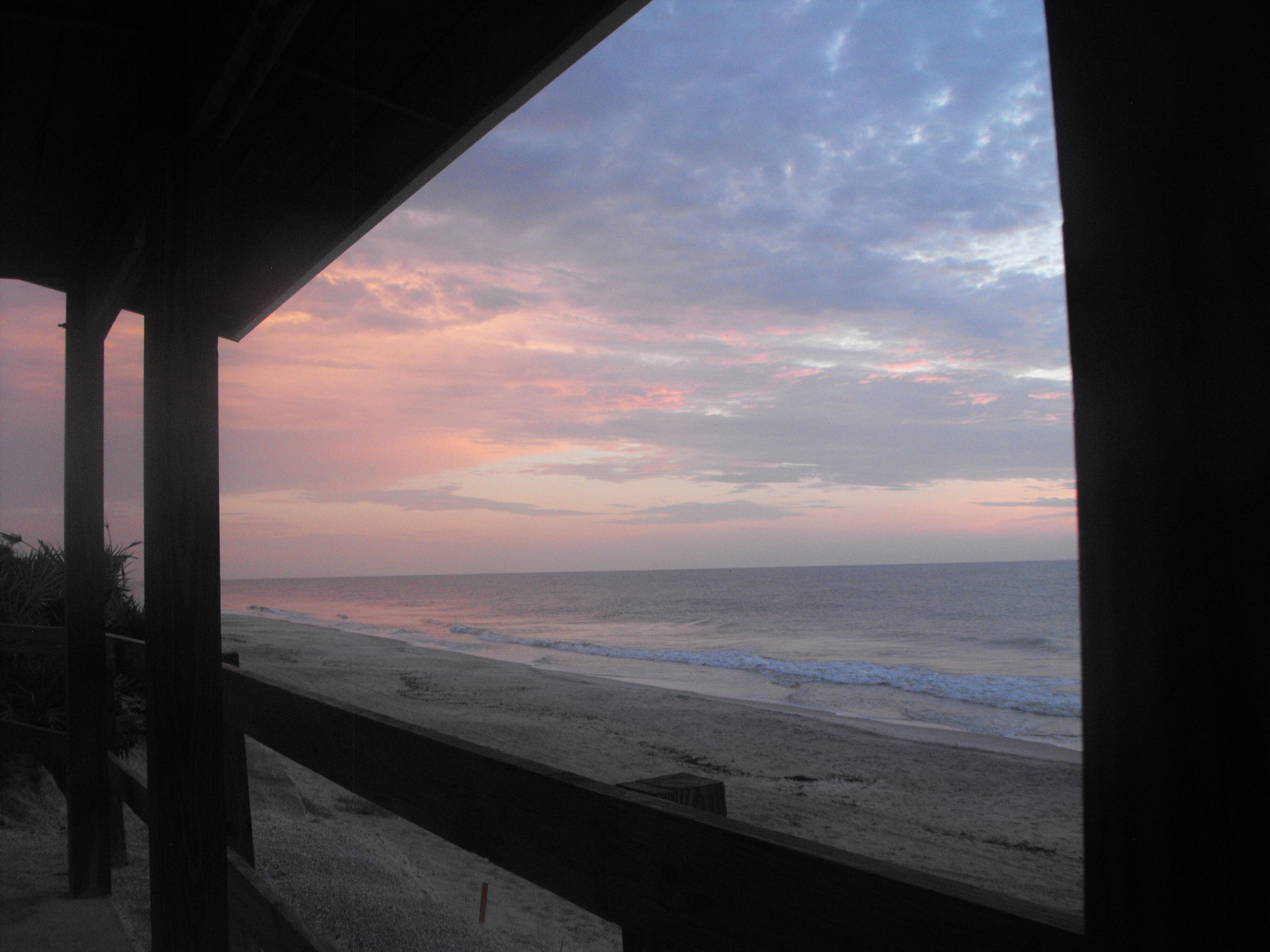 A beach view from a covered area with wooden pillars.