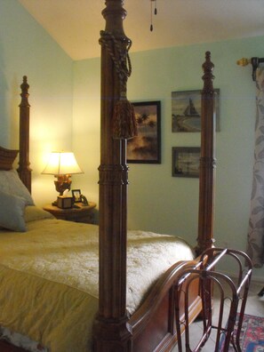 A bedroom with a four-poster bed, a bedside lamp, and a framed picture on the wall.