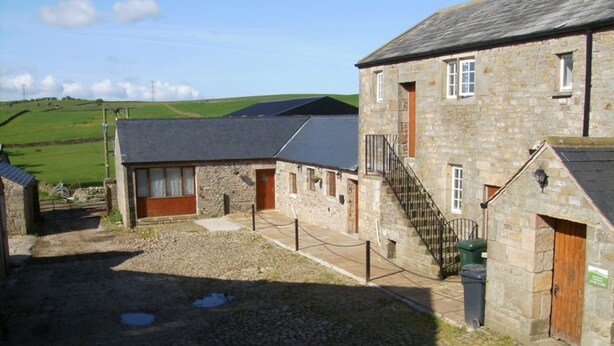 A stone building with a courtyard, a staircase, and a view of green fields. - Clougha View (Lancaster)