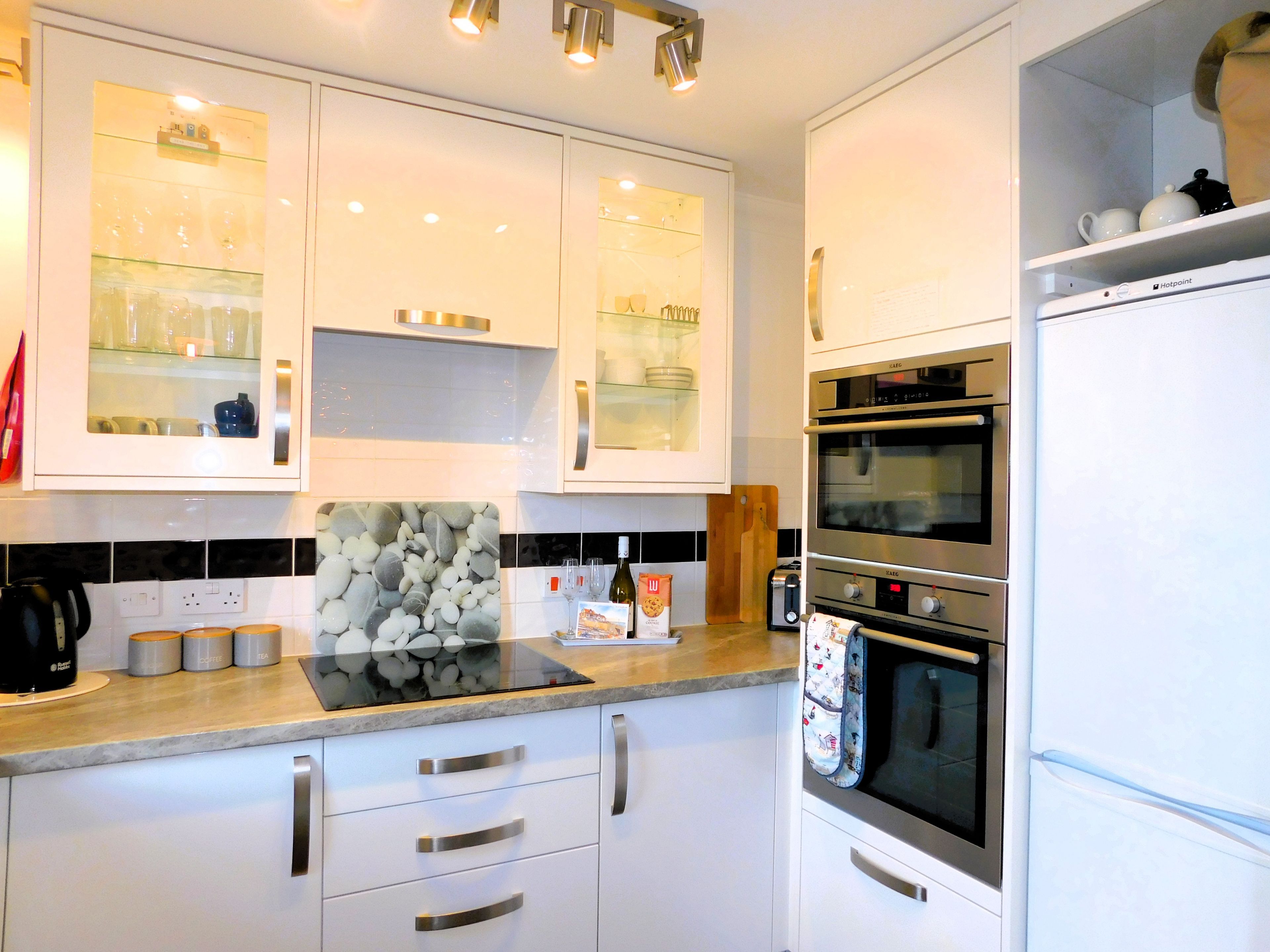 A modern kitchen with white cabinets, a built-in oven, and a coffee machine.