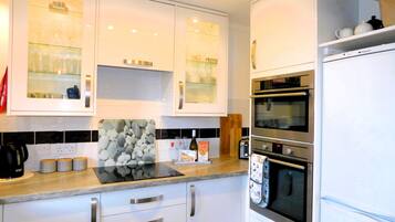 A modern kitchen with white cabinets, a built-in oven, and a coffee machine.